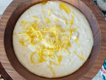 Top down view of white bean dip with lemon zest on top in a wood bowl.