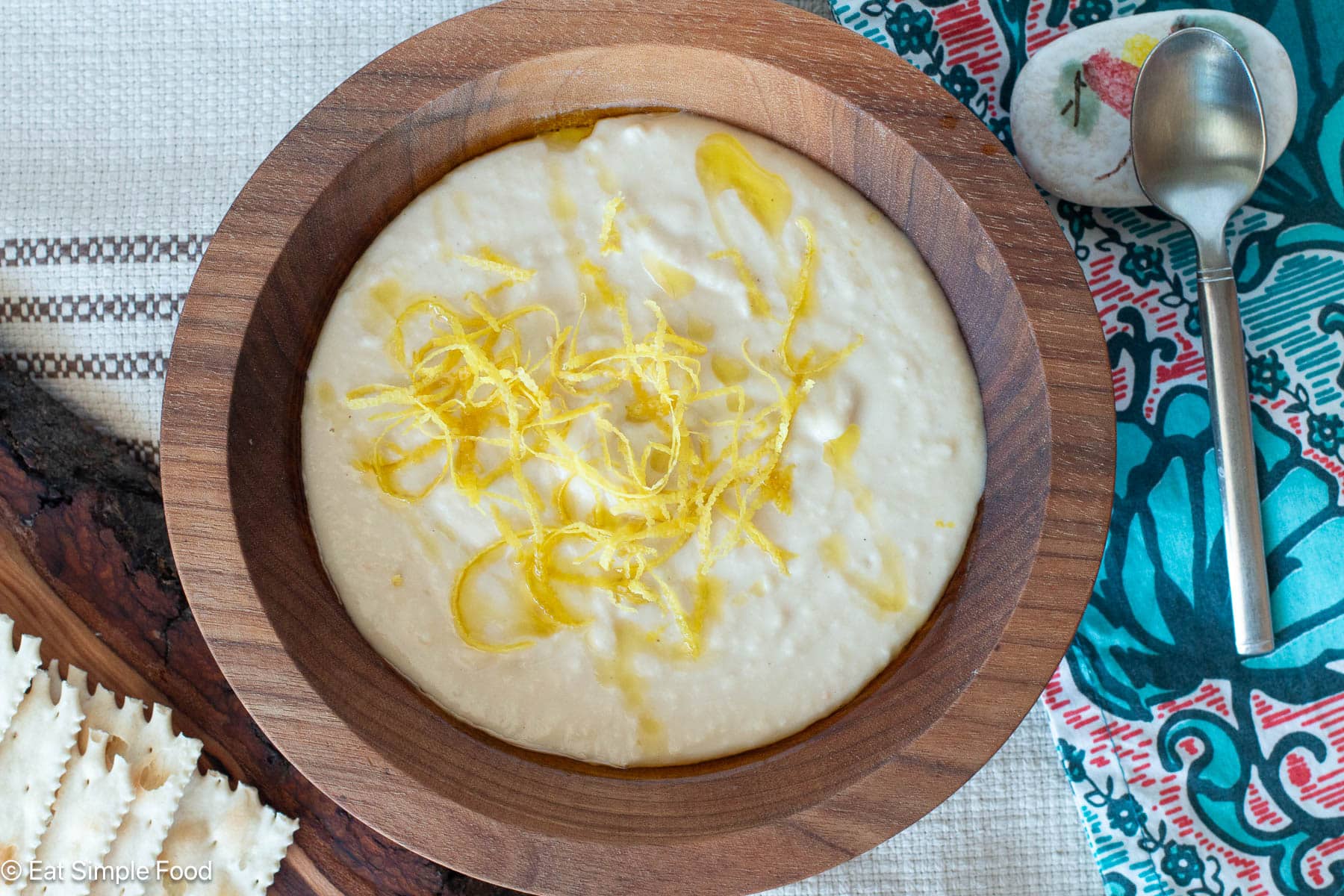 Top down view of pureed white dip with lemon zest in a wood bowl. Spoon and crackers on the side.