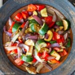 Top down view of chunky cooked onions, zucchini, peppers on a brown plate with white napkin in background. Close up.