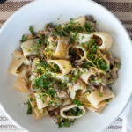 Top down view of pasta on a white plate. Pasta is filled with ingredients and has lemon zest and parsley on the top.