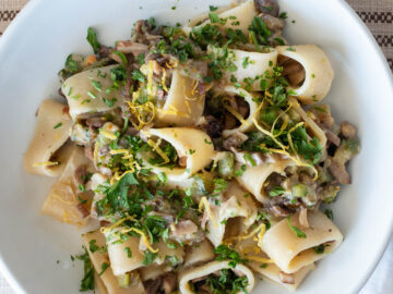 Top down view of pasta on a white plate. Pasta is filled with ingredients and has lemon zest and parsley on the top.