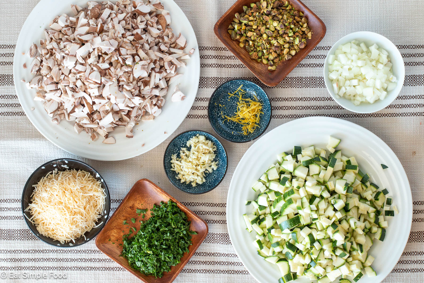 Top down view of ingredients on white plates, square wood containers, and colorful bowls. Ingredients are chopped, diced, grated, and minced.