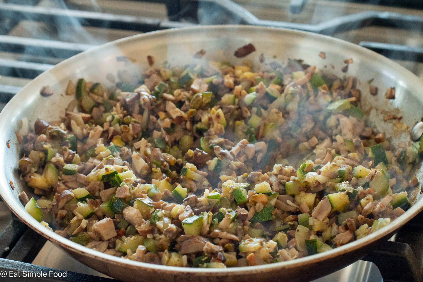 Stainless steel pan of chopped ingredients cooking on a gas stove top.