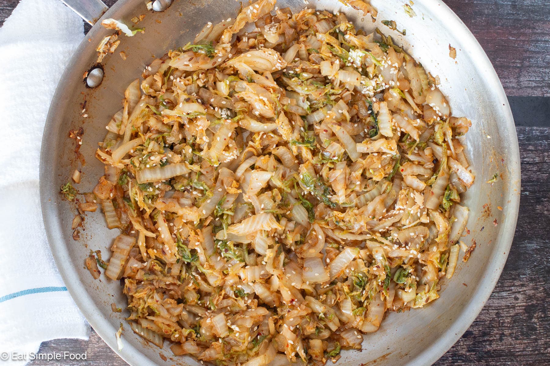 Top down view of cooked greens in a stainless steel pan with a white bar towel on the side.