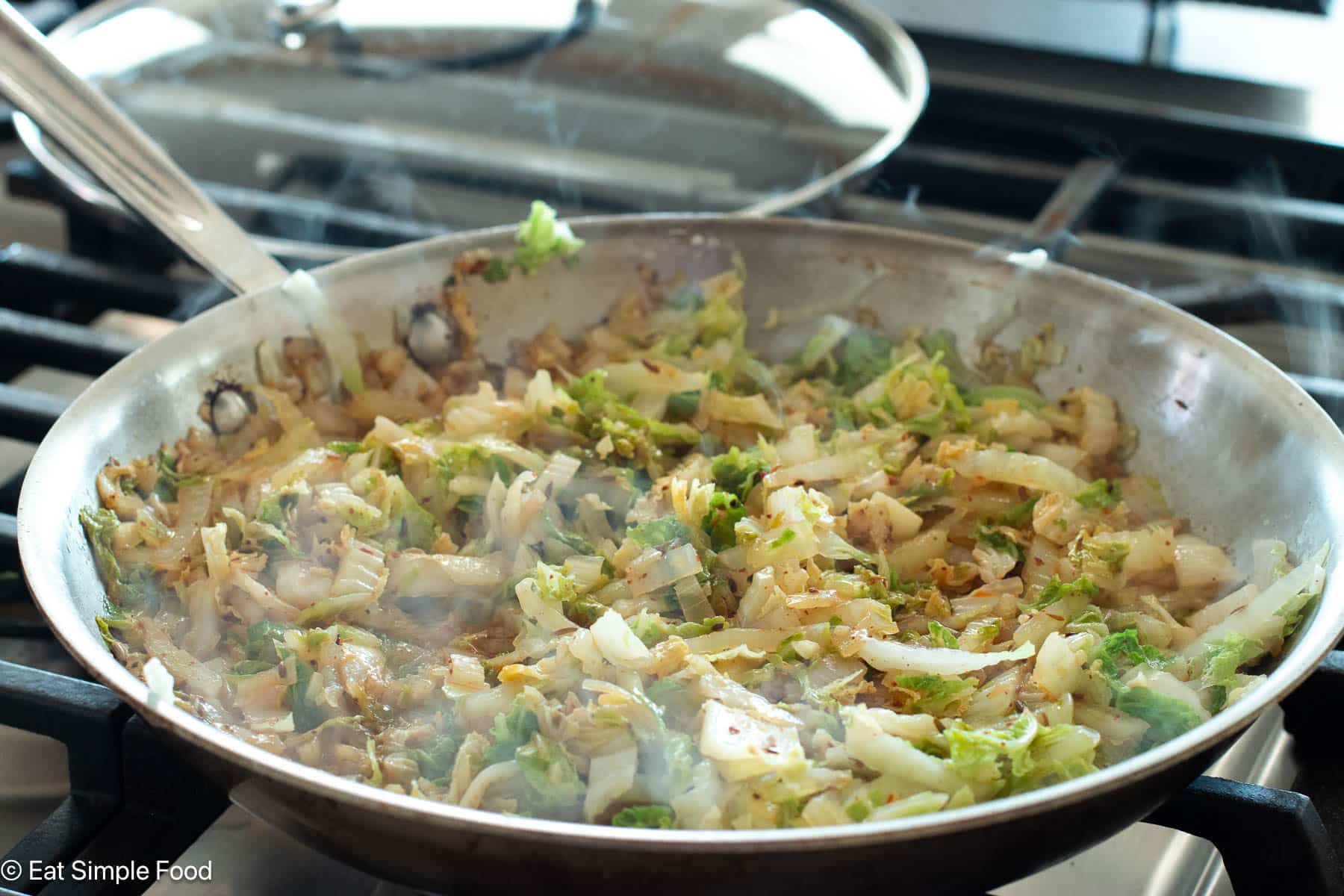 Side view of cabbage cooking on a gas stove top in a stainless steel pan.