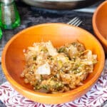 Close up of wood bowl filled with cooked cabbage slices and topped with sesame seeds with a fork in the bowl. Salt and pepper shakers in background.