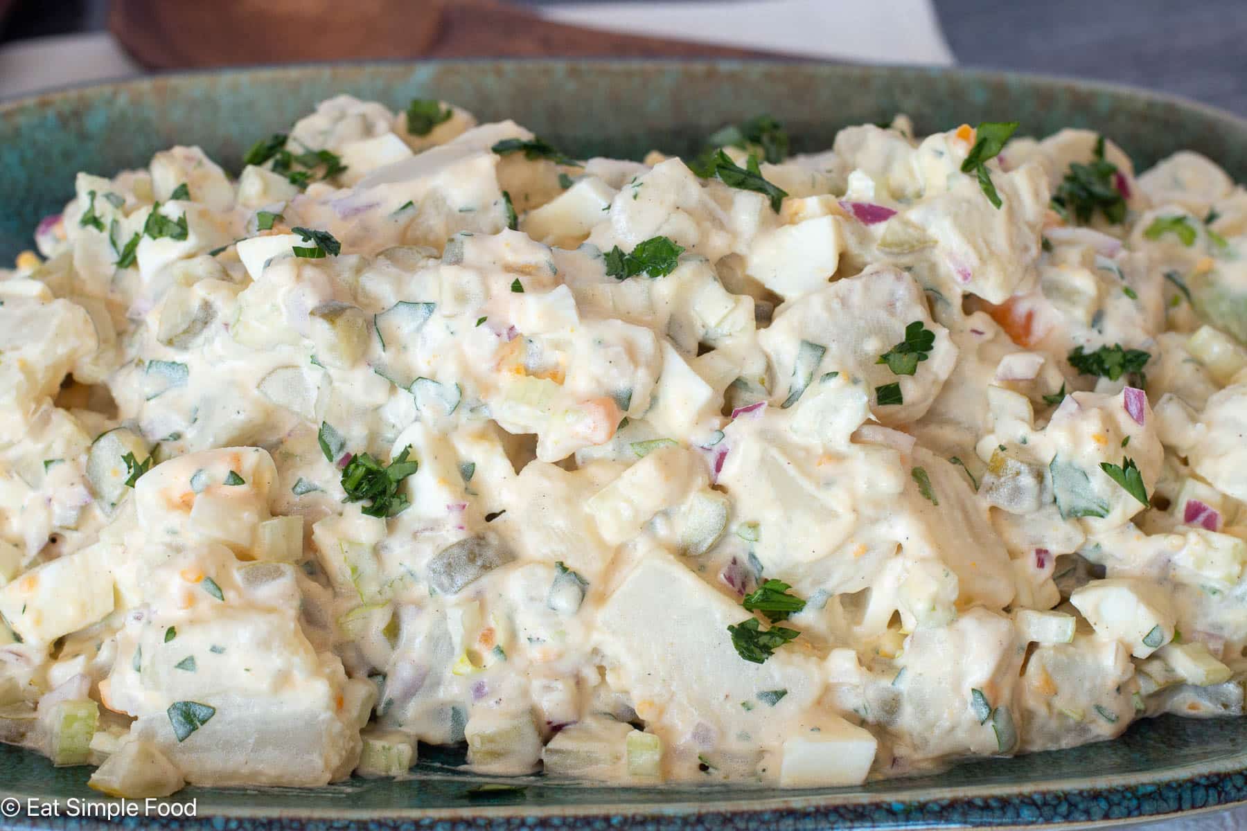 Close up side view of potato egg salad on an aqua plate.