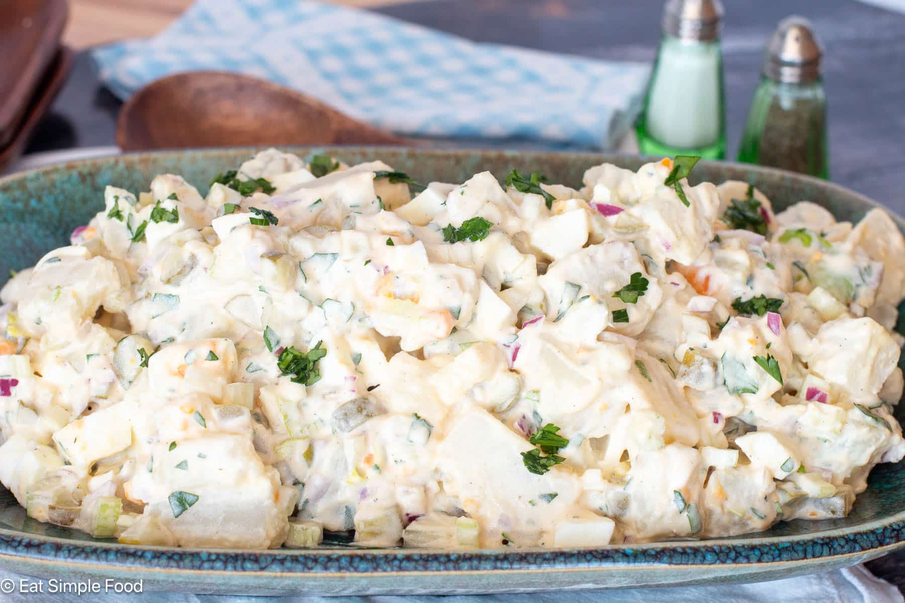 Side view of creamy potato salad on aqua plate with green salt and pepper shakers in the background.