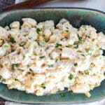 top view of potato salad on a square aqua plate with utensils on the side. Close up view.