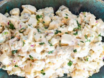 top view of potato salad on a square aqua plate with utensils on the side. Close up view.