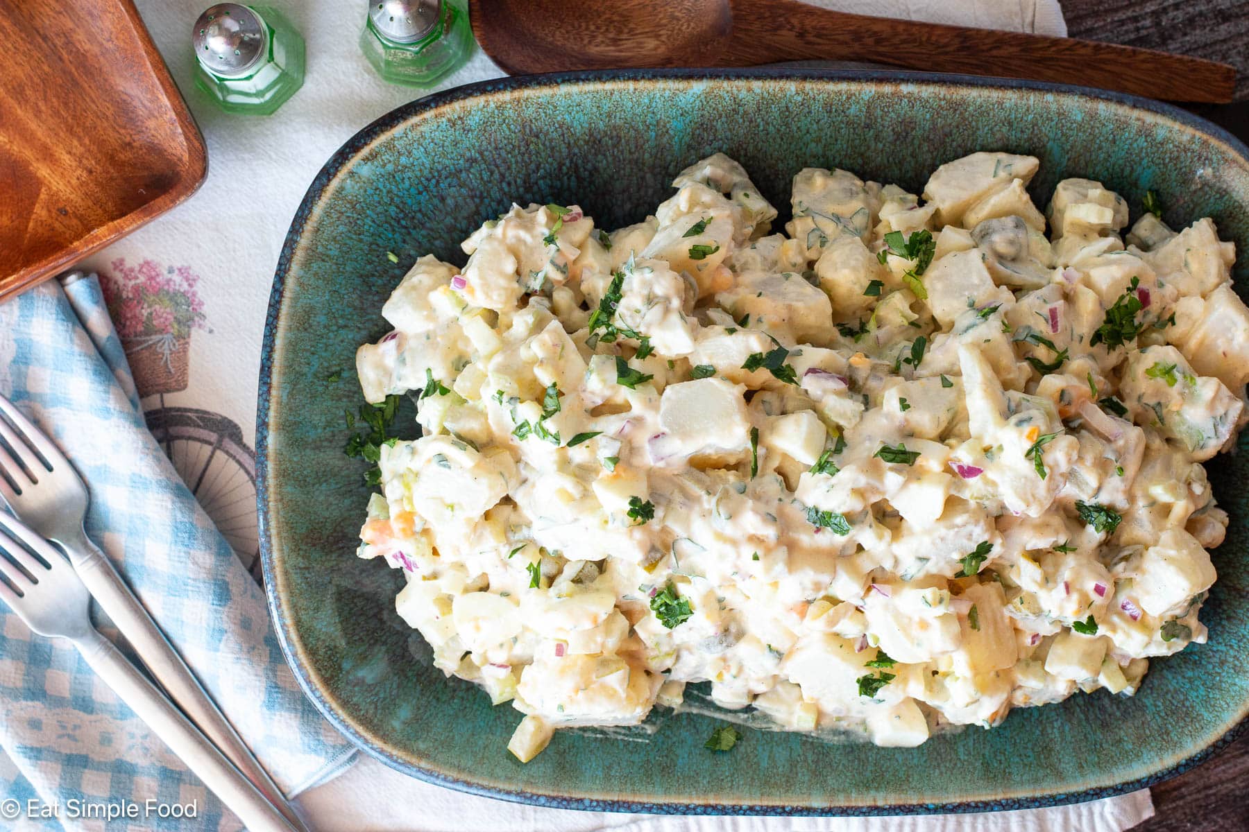 top view of potato salad on a square aqua plate with utensils on the side.