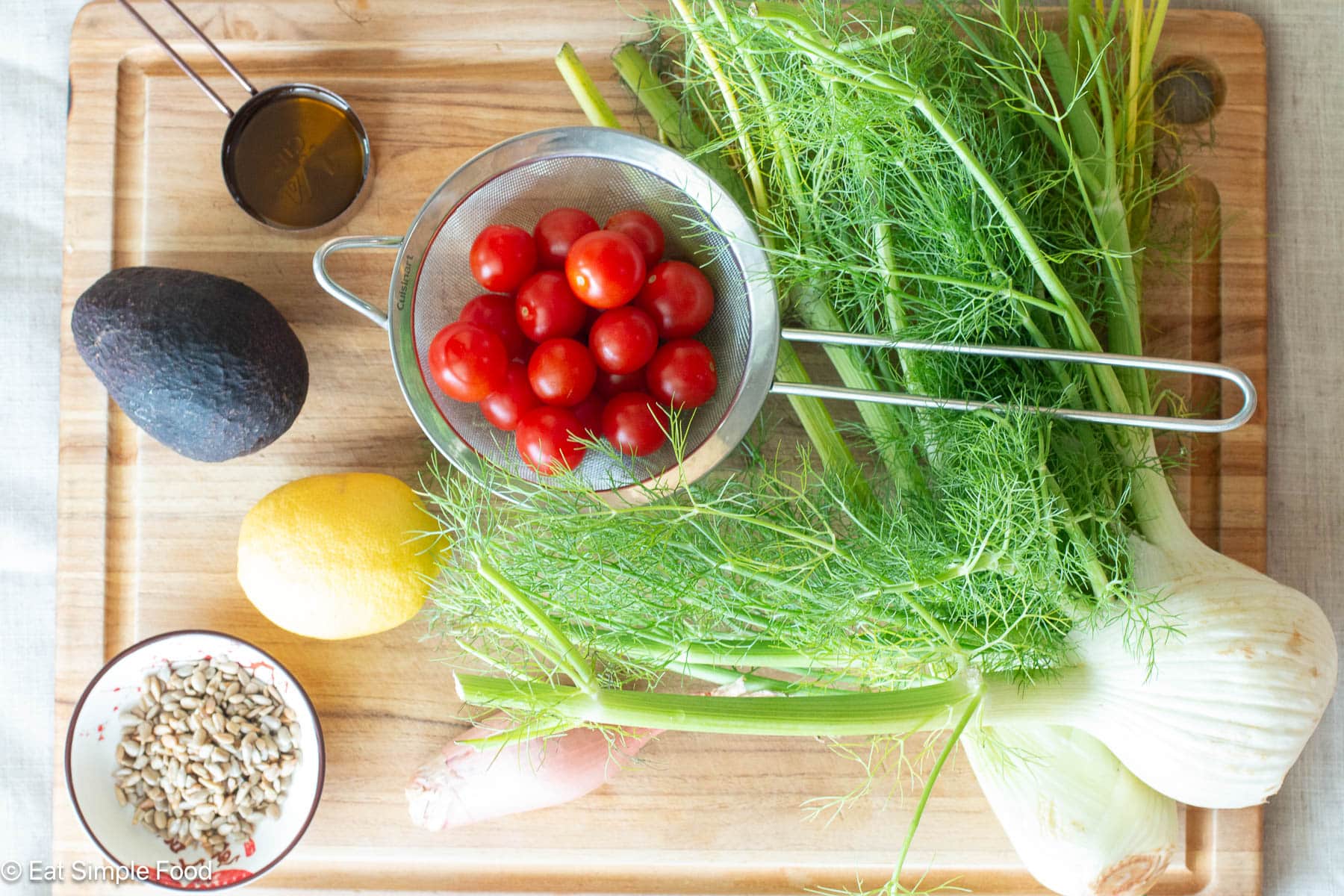 Top down view of fennel, cherry tomatoes, a lemon, an avocado, a shallot and sunflower seeds.