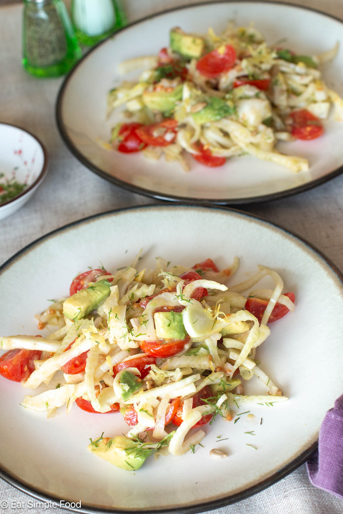 Two white plates of salad with salt and pepper shakers