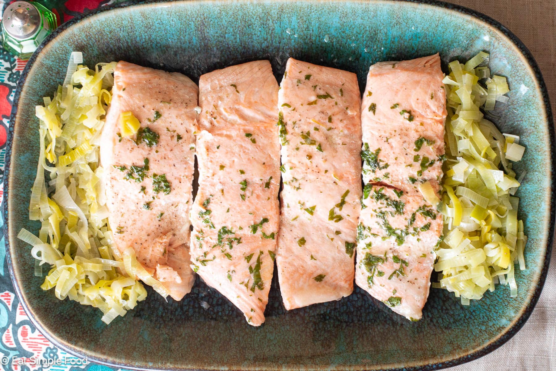 4 pieces of salmon on an aqua platter with sliced cooked leeks on the side of plate.