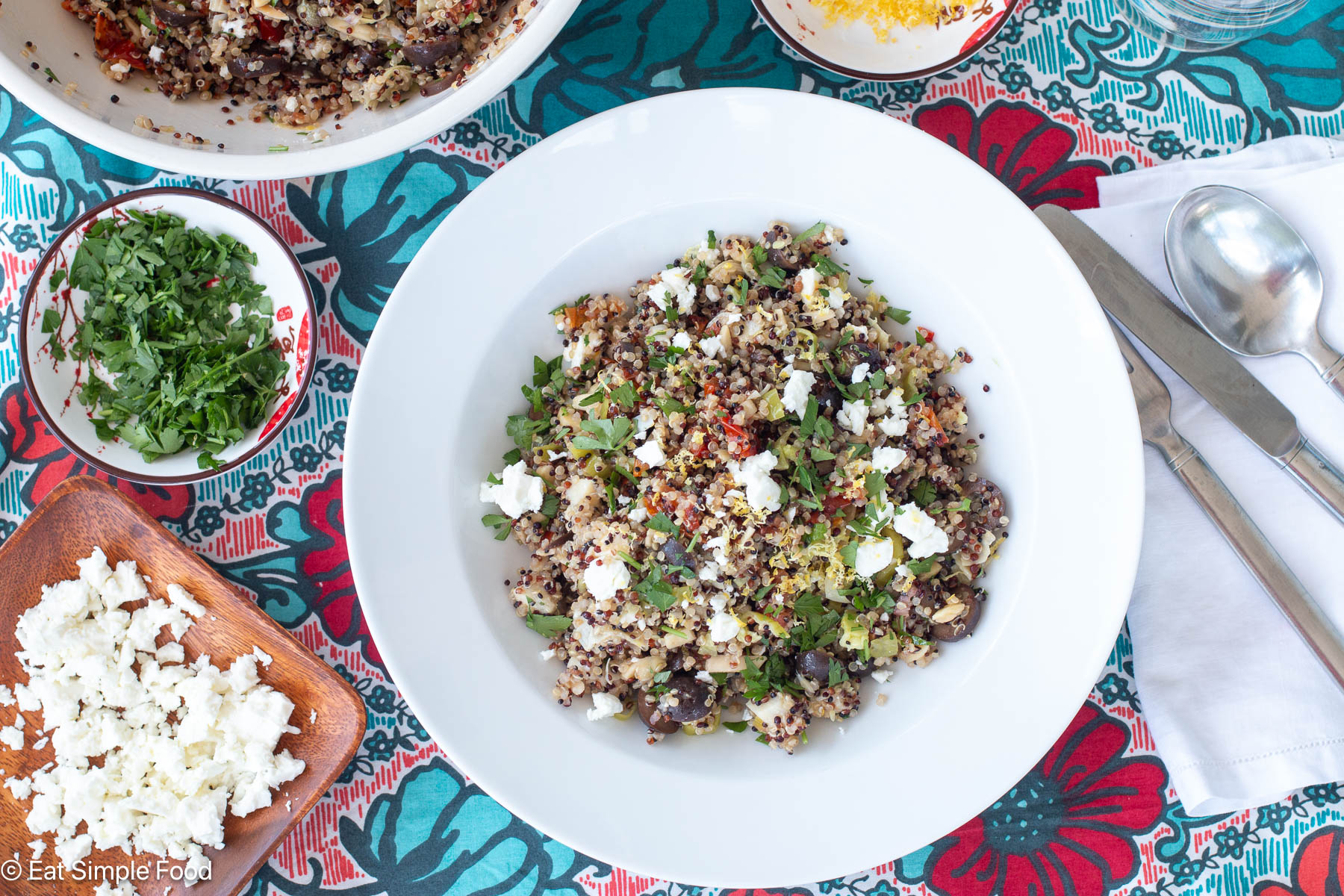 Top down view of grain salad with feta cheese on a colorful table runner. Silverware on the side on a white napkin.