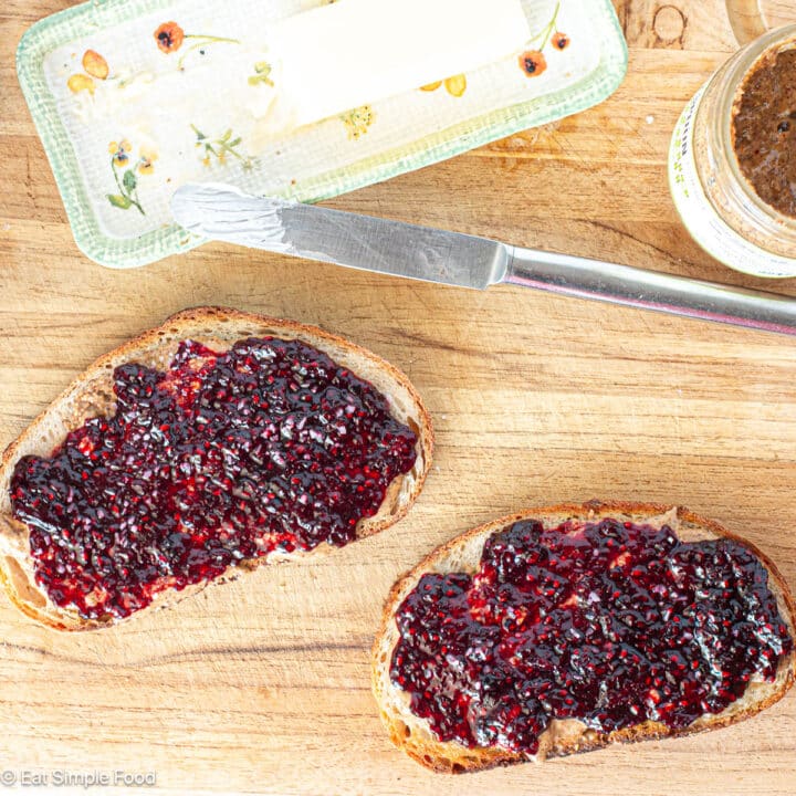 Close up and top view of two pieces of toast with blackberry jam. Butter and peanut butter and jelly jar on the side.