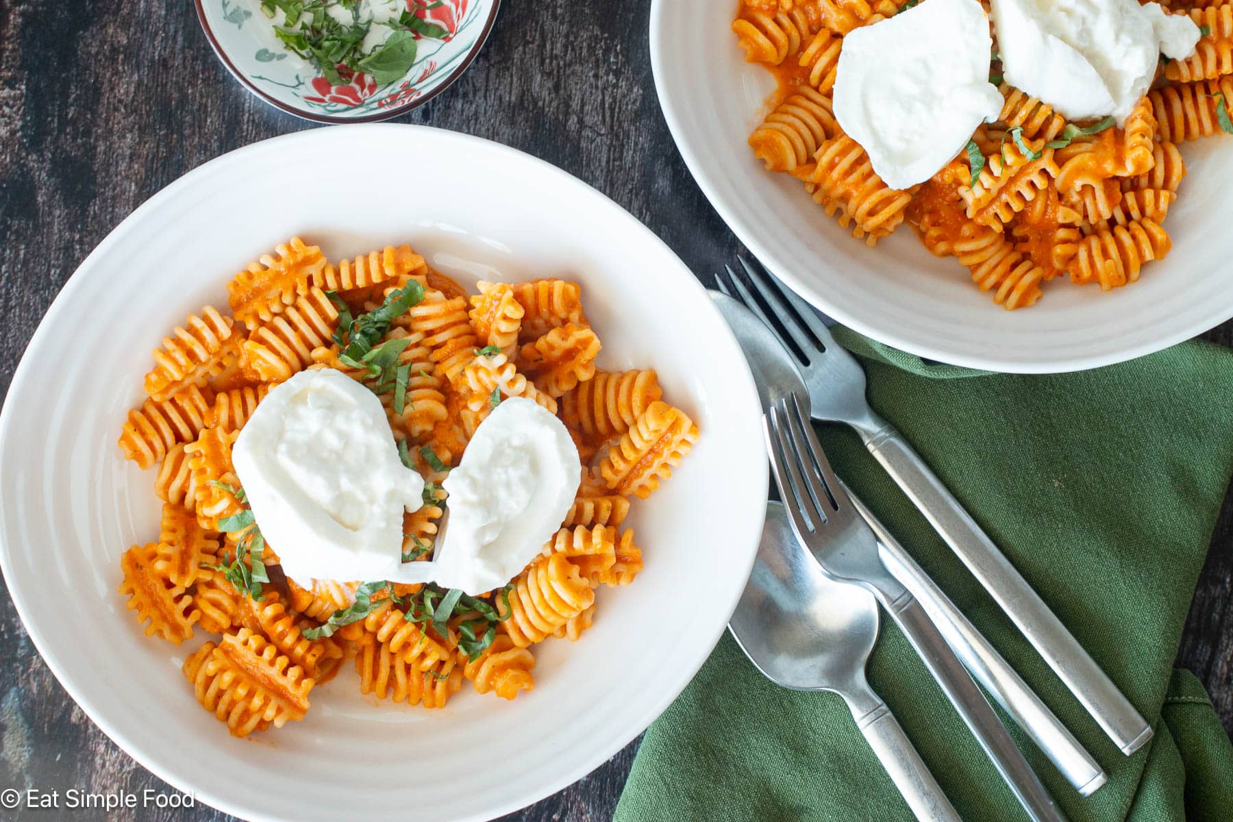 Top down close up view of two plates of pasta in red sauce with with cheese on top, green napkins and silverware on the side.