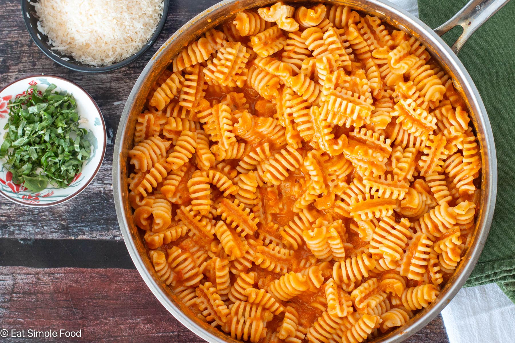 Top down view of pan full of pasta in red sauce with basil and cheese on the side.