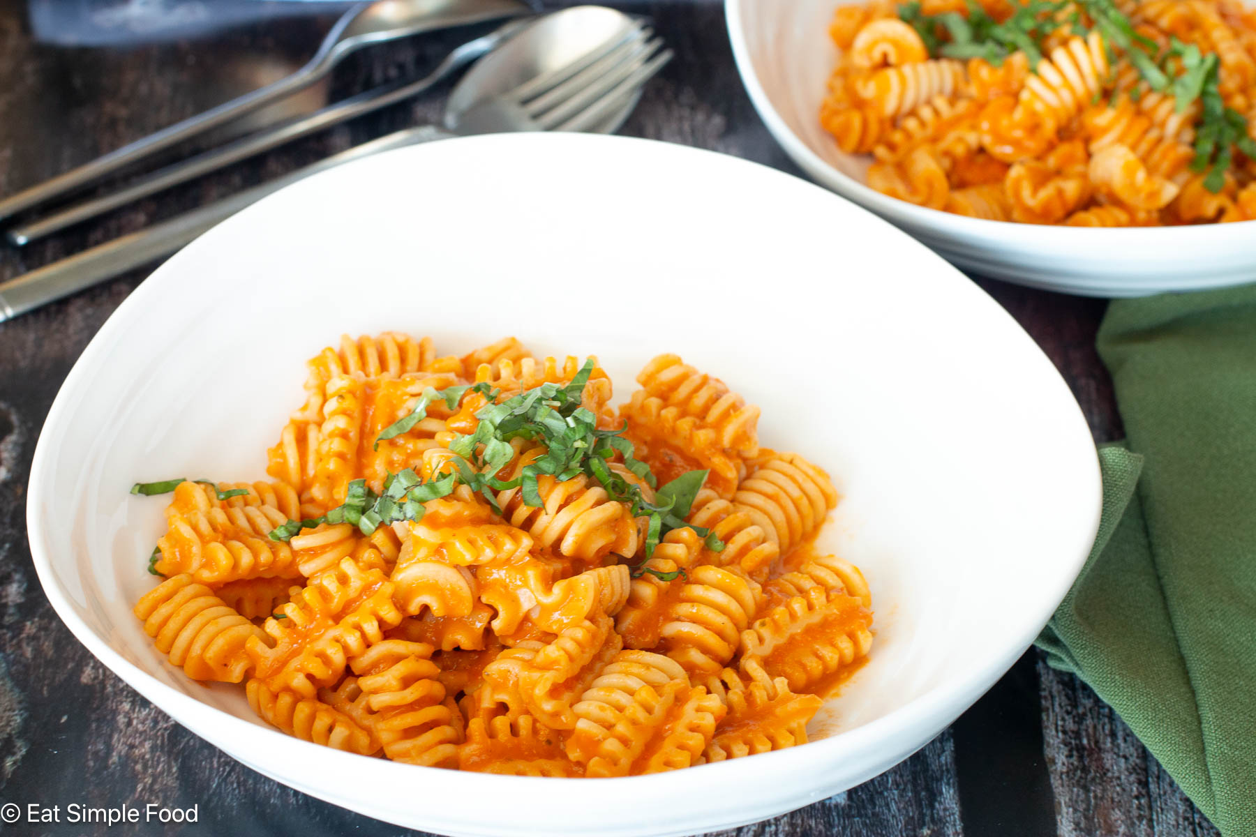Side view of pasta in tomato sauce in a white plate with basil on top and a green napkin.