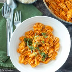 Top down view of pasta in tomato sauce in a white plate with basil on top and a green napkin.