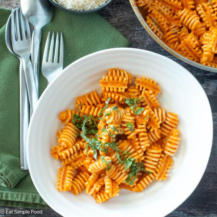Top down view of pasta in tomato sauce in a white plate with basil on top and a green napkin.