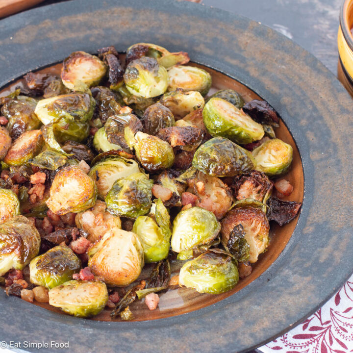 Roasted Brussels Sprouts halves on a brown plate with cooked bacon. Side view. Close up.